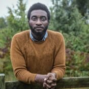 Pensive young man Tolulope Olajide leaning on a wooden fence whilst on his walk through the woodlands