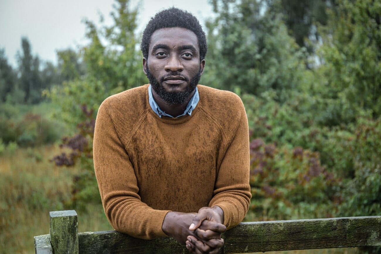 Pensive young man Tolulope Olajide leaning on a wooden fence whilst on his walk through the woodlands