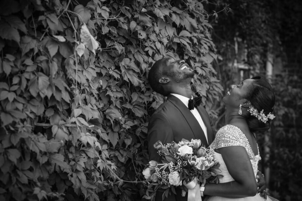 Stunning wedding photo of Chidinma and Tolulope Olajide in the garden. Black and white picture. Both throwing their head backwards filled with joy and laughter