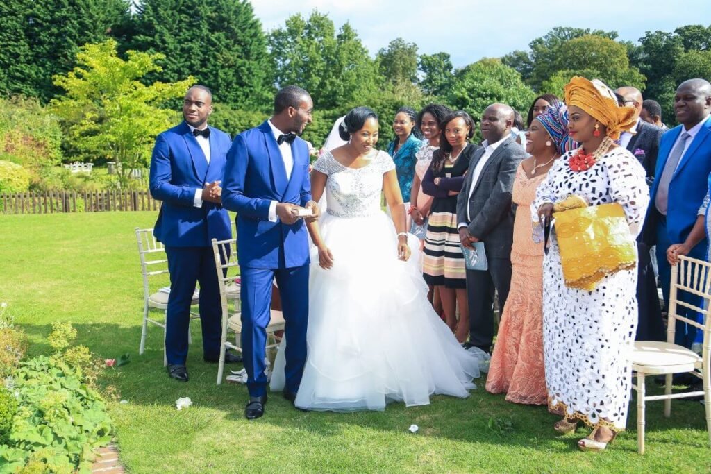 Newlywed Tolulope and Chidinma Olajide smiling in view of a section of guests at the beautiful outdoor wedding. sunshine