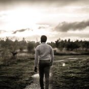 A young millennial man walking through a meadow on a gravelled path