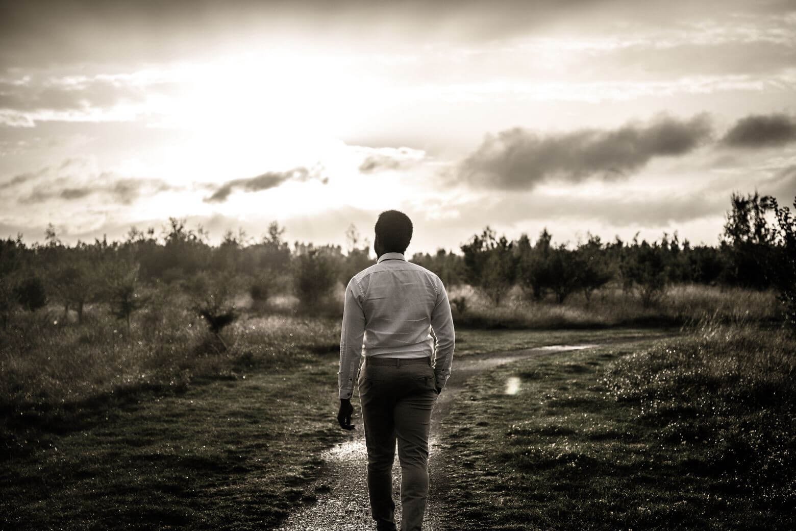 A young millennial man walking through a meadow on a gravelled path