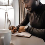 African young man Tolulope Olajide in black turtle neck, writing into his journal about Can One escape anxiety during the grieving process?