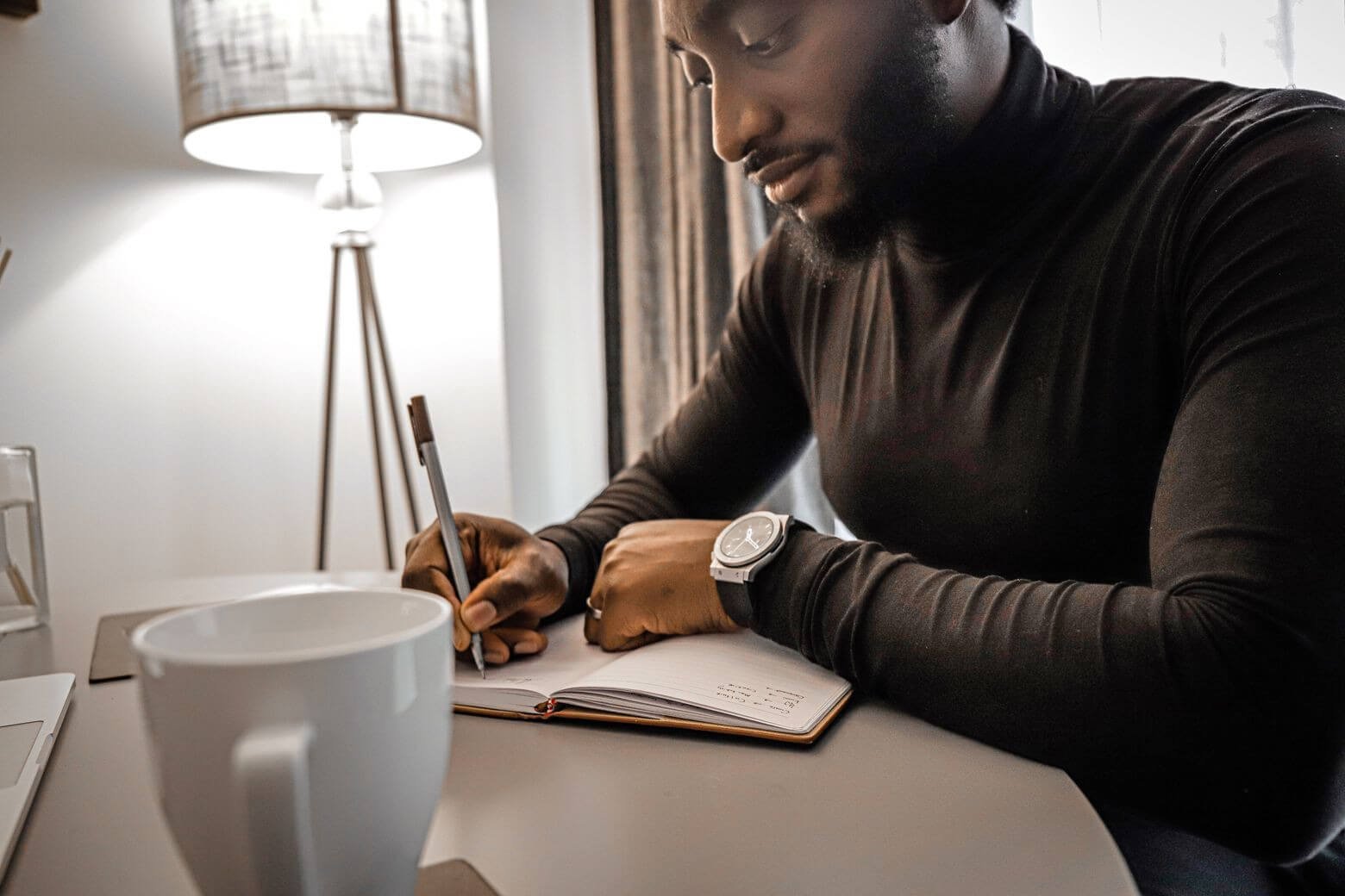 African young man Tolulope Olajide in black turtle neck, writing into his journal about Can One escape anxiety during the grieving process?